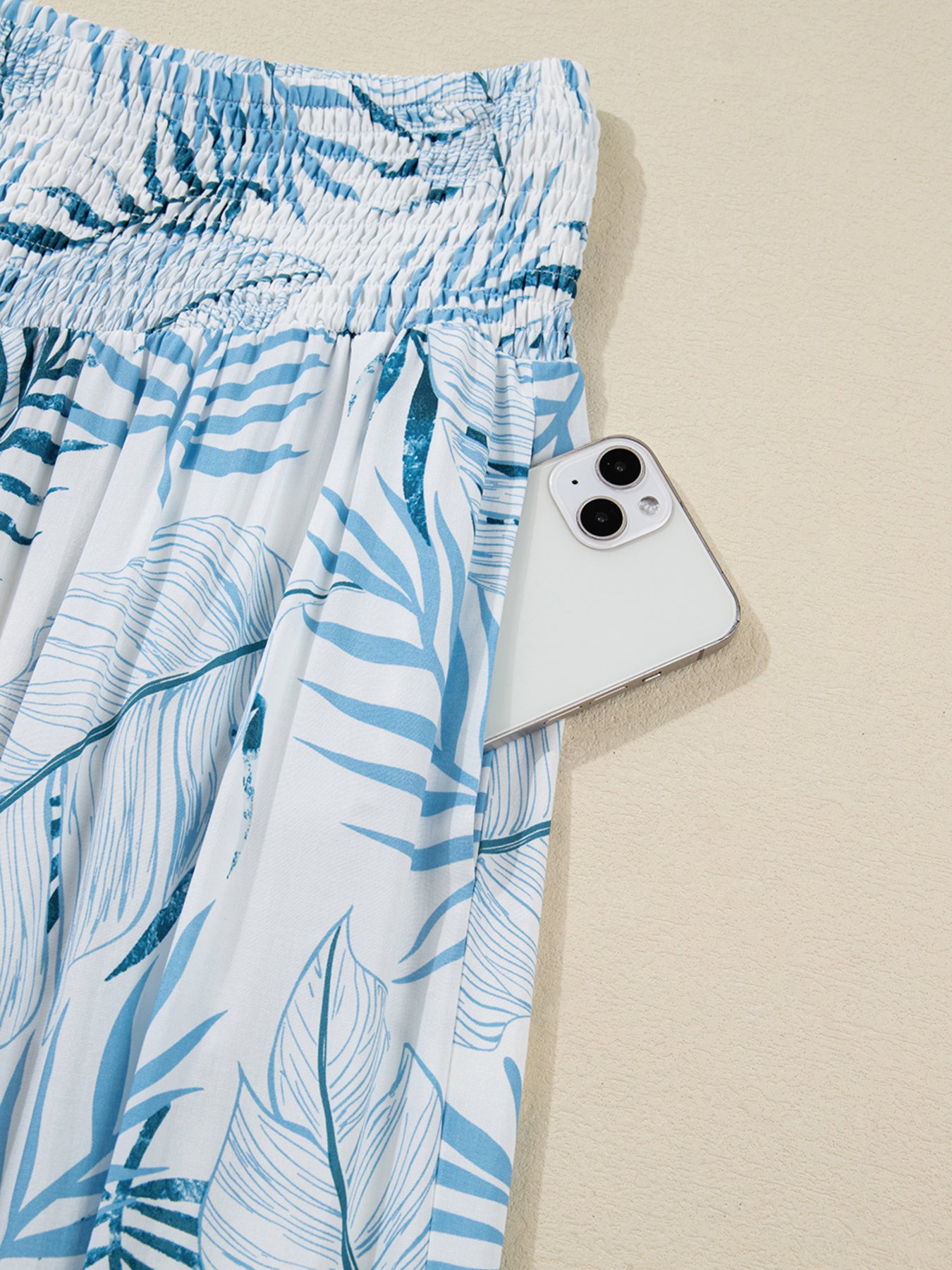 Blue leaf-patterned skirt with a white phone on a beige background
