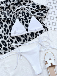 White bikini set on a leopard print blanket with a sandal beside it.