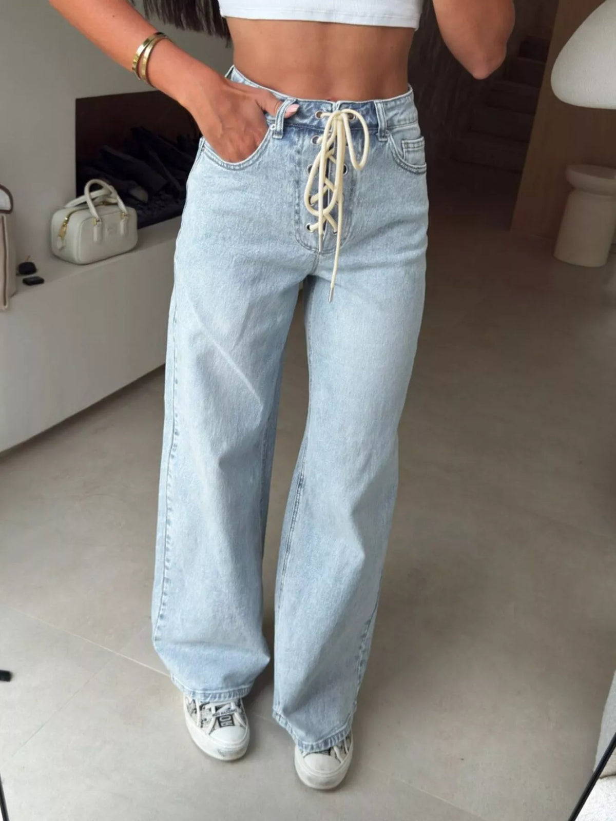 Person wearing high-waisted light blue jeans with lace-up detail indoors.