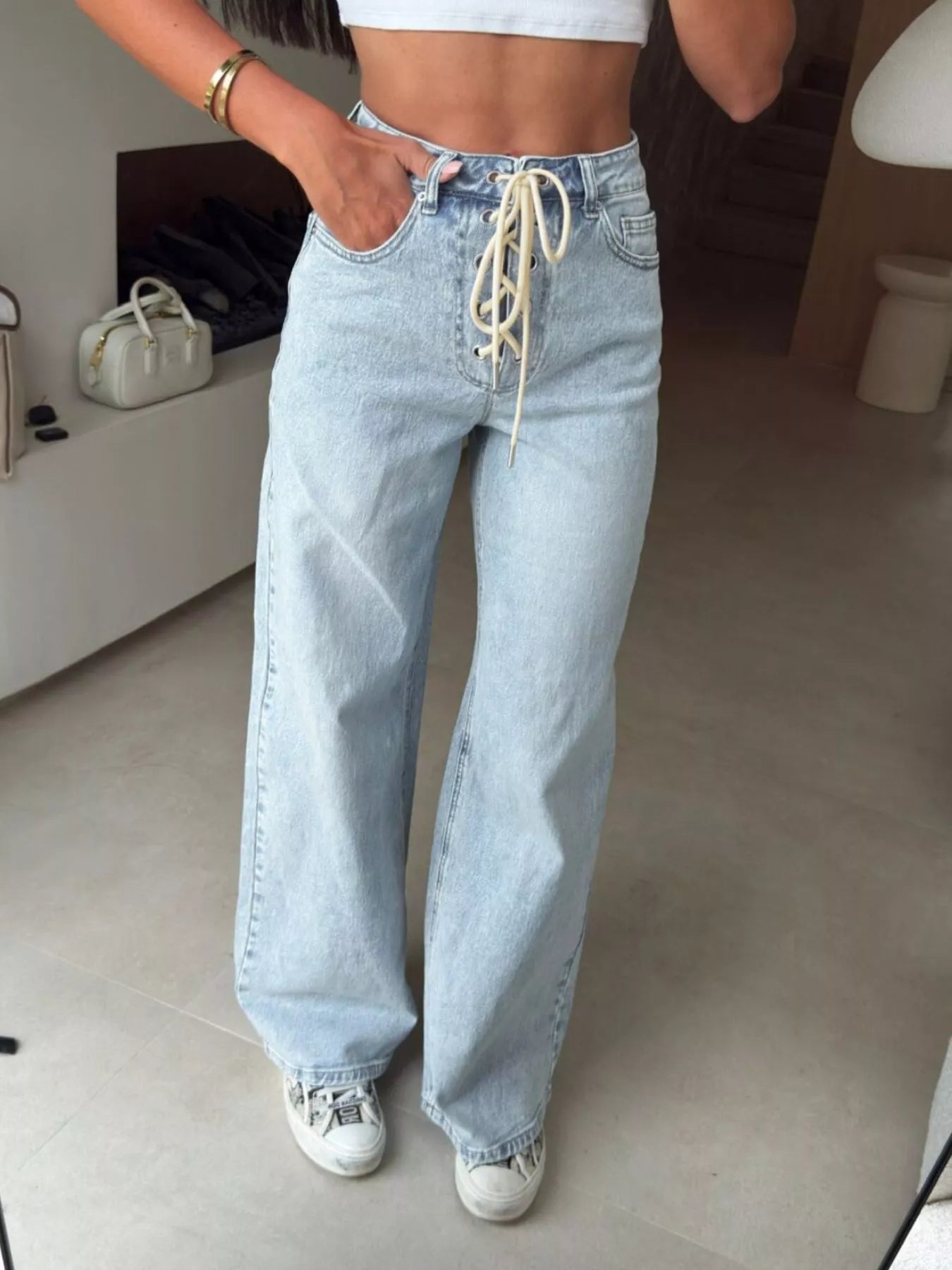 Person wearing high-waisted light blue jeans with lace-up detail indoors.