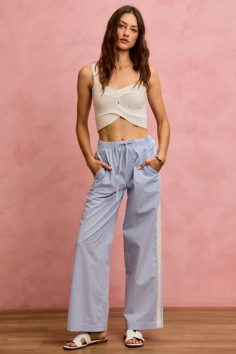 Woman wearing a beige top and light blue checkered pants against a pink background