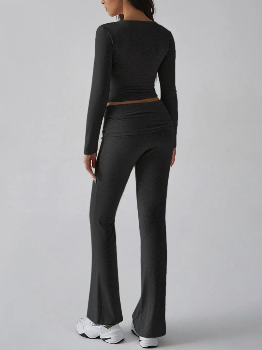 Person wearing a black long-sleeve crop top and flared pants on a gray background