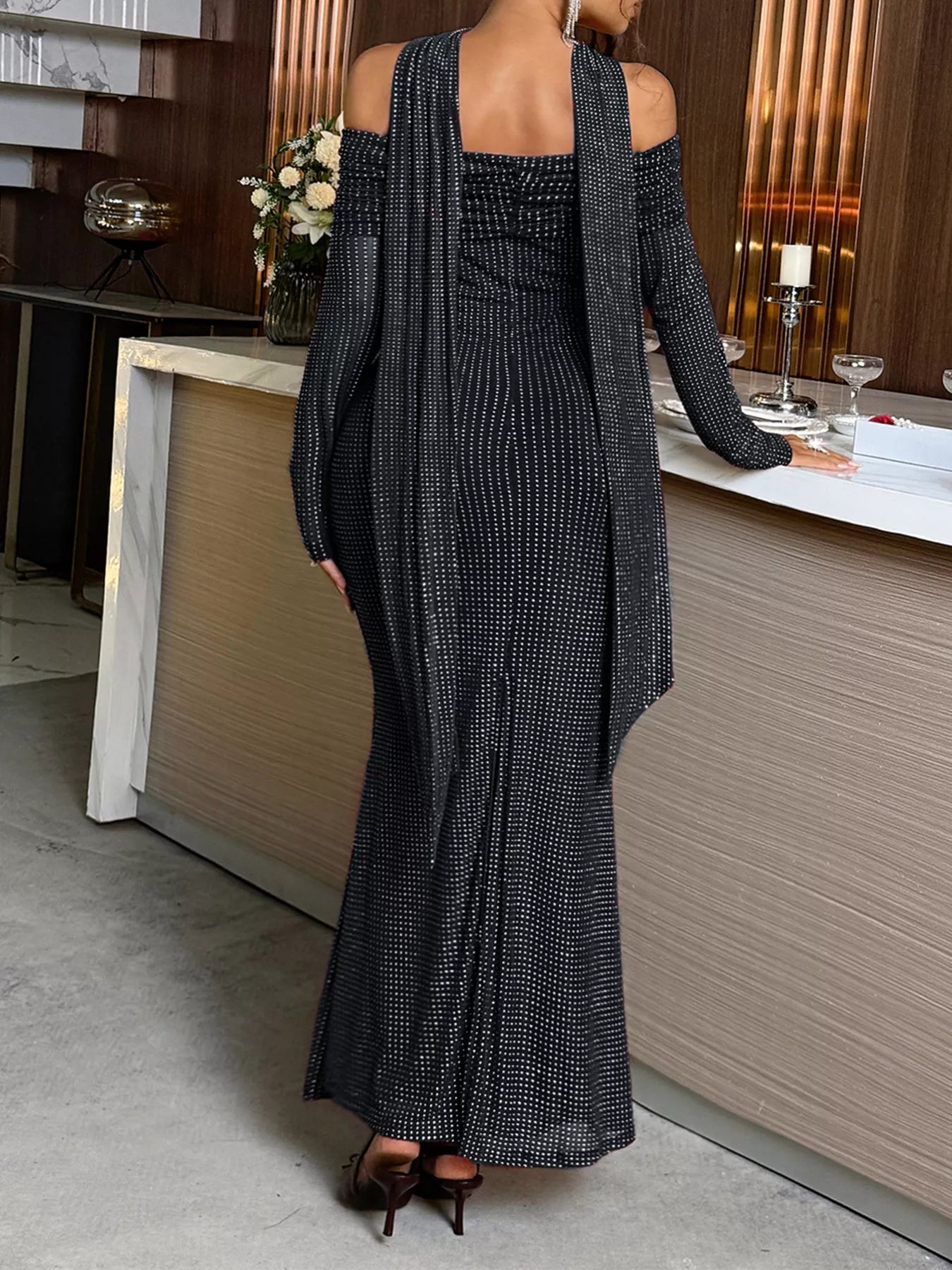 Person wearing a long black dress with a textured pattern in an indoor setting.