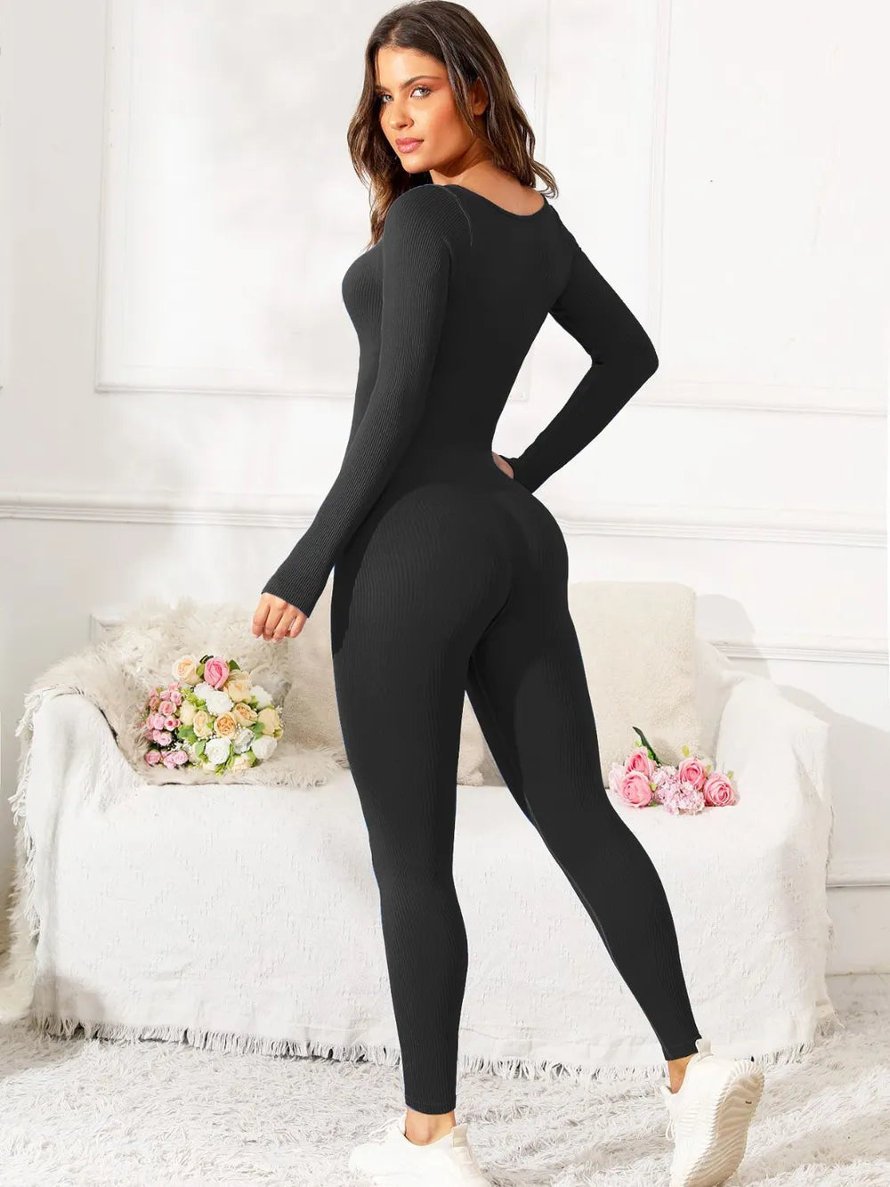 Woman wearing a black bodysuit in a room with white walls and decorative elements.
