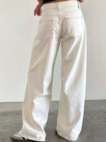 A person wearing off-white wide-leg jeans, shown from the back, standing against a plain light gray wall and concrete floor.