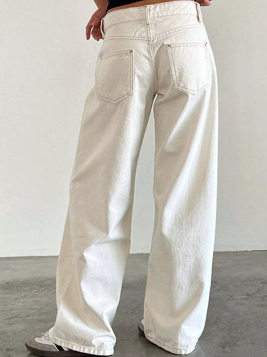 A person wearing off-white wide-leg jeans, shown from the back, standing against a plain light gray wall and concrete floor.