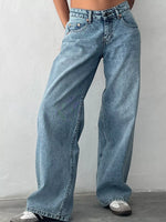 A person wearing light blue wide-leg denim jeans with a faded wash, paired with white sneakers, standing against a light gray wall.