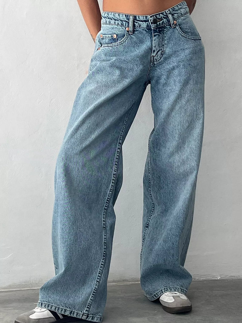 A person wearing light blue wide-leg denim jeans with a faded wash, paired with white sneakers, standing against a light gray wall.