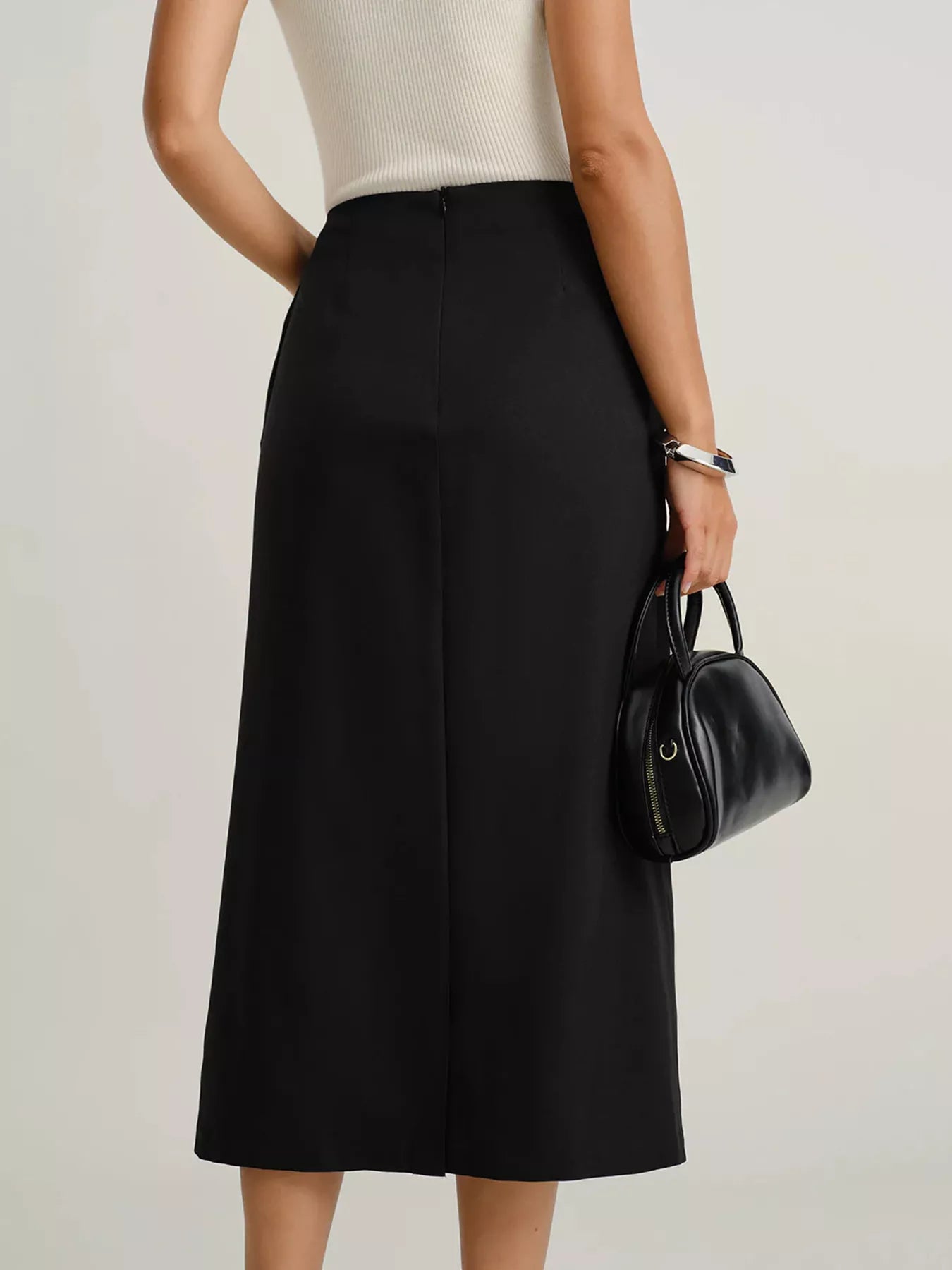 Person wearing a black skirt and holding a black handbag on a plain background