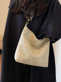 Beige handbag held by a person wearing a black outfit against a neutral background