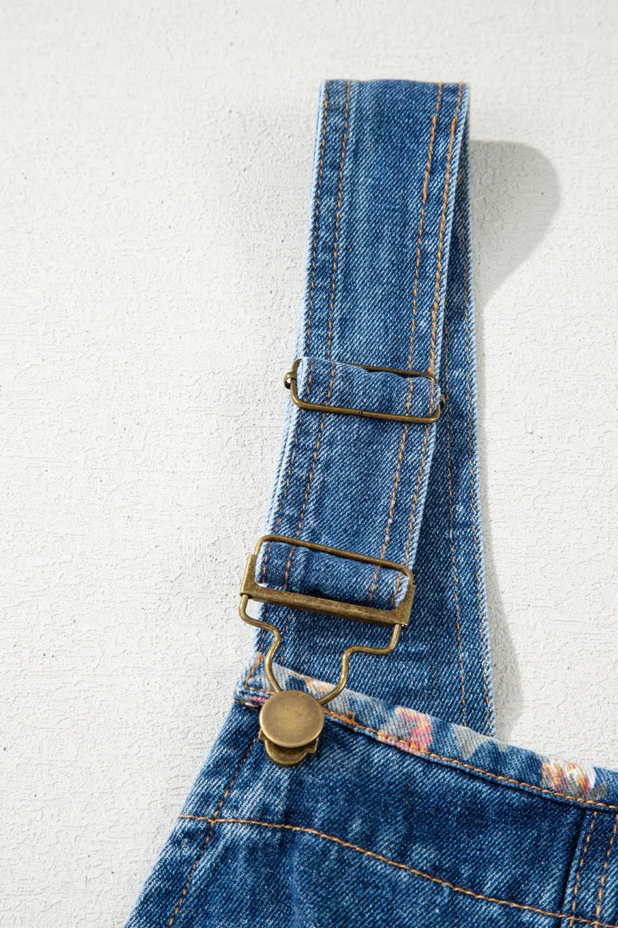 Close-up of blue denim overalls with floral pattern on a light gray background
