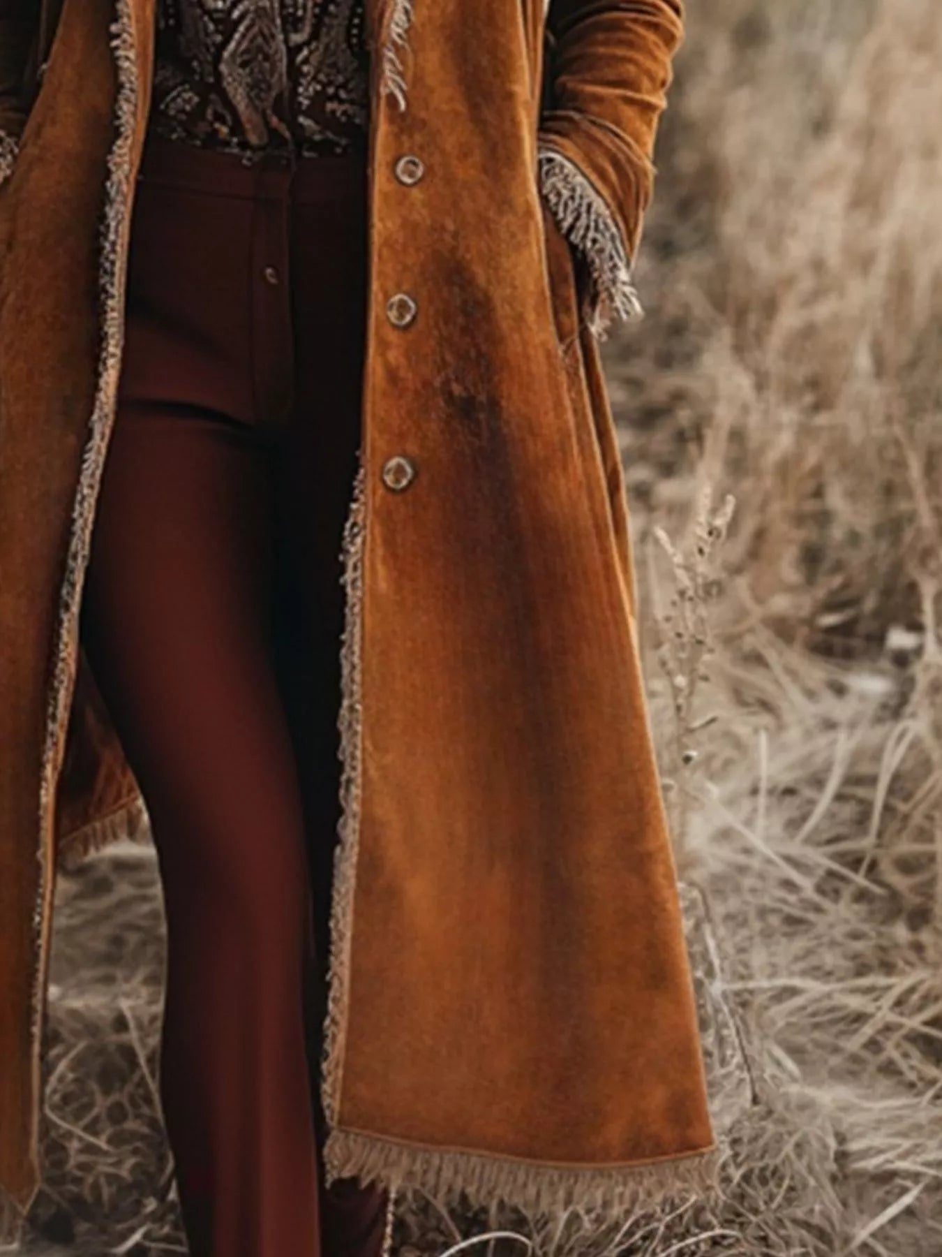 Person wearing a long brown suede coat with fringes in a natural setting