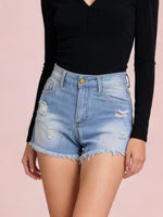 Person wearing a black long-sleeve top and light blue denim shorts on a pink background