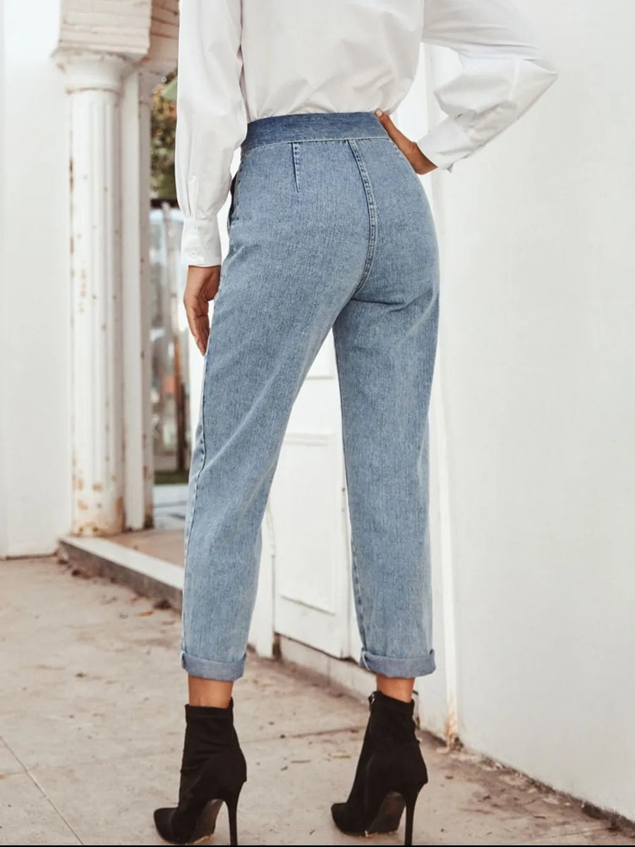 Person wearing light blue jeans and black ankle boots standing on a sidewalk.