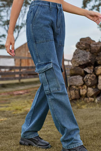 Person wearing blue jeans standing outdoors with a wooden fence and stacked logs in the background