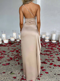 Woman in a beige evening gown standing in front of candles and rose petals on a floor.