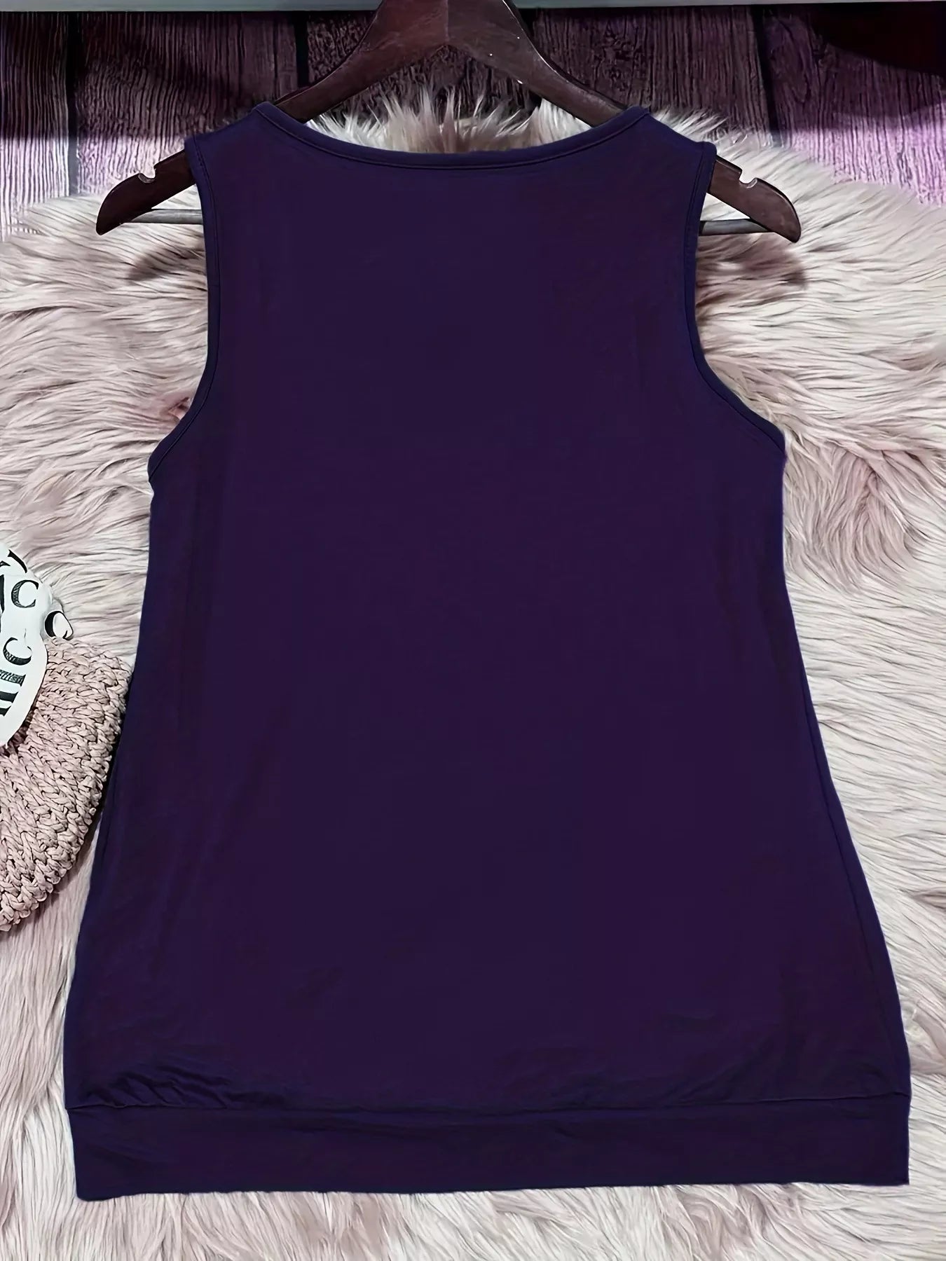 Purple tank top on a hanger against a textured white surface