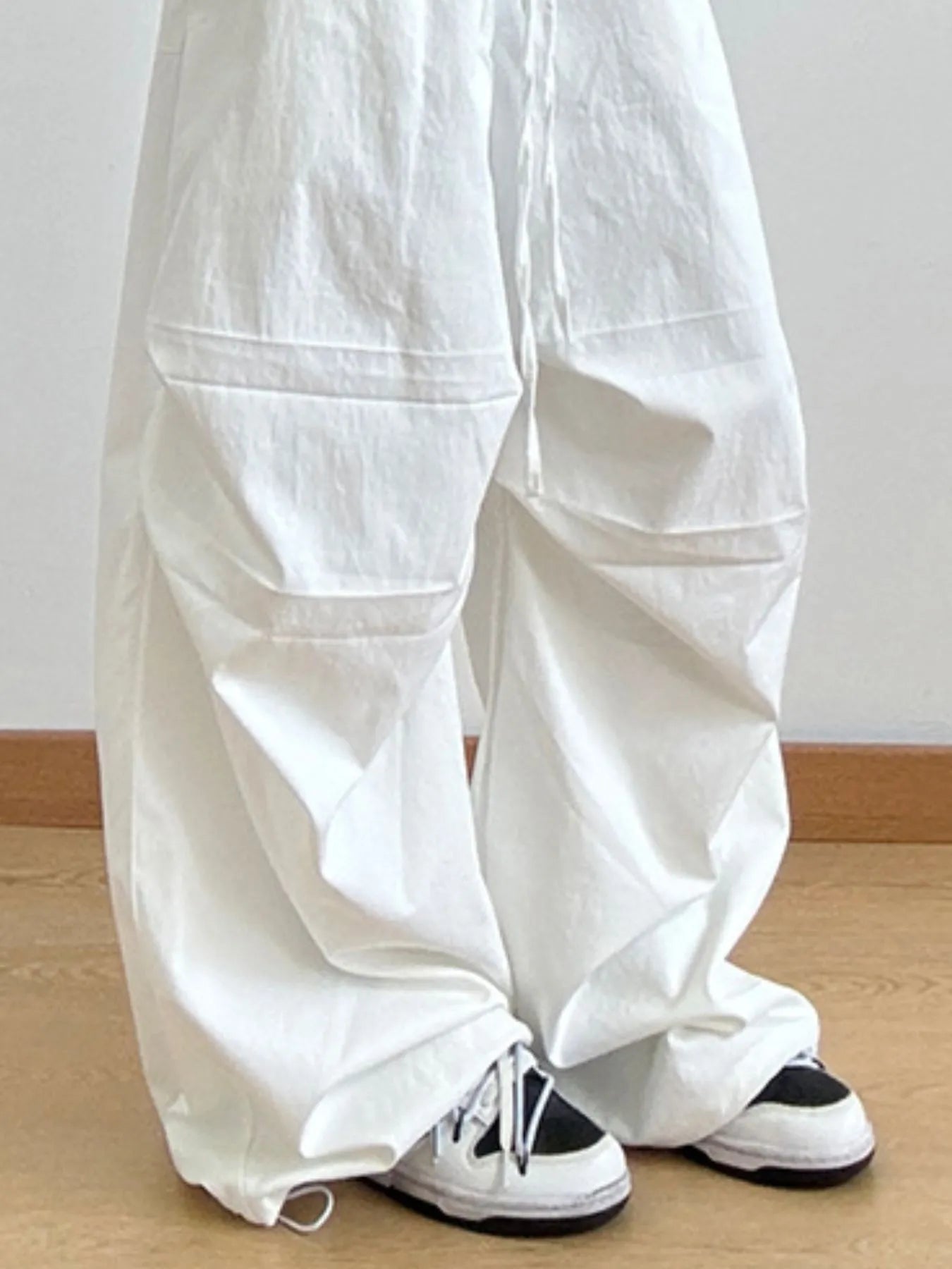 White wide-leg pants worn by a person on a wooden floor with a white wall background