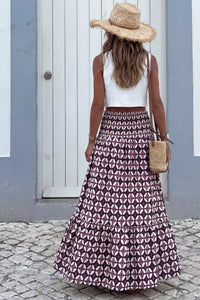 Woman wearing a patterned skirt, white top, and straw hat in an urban setting.