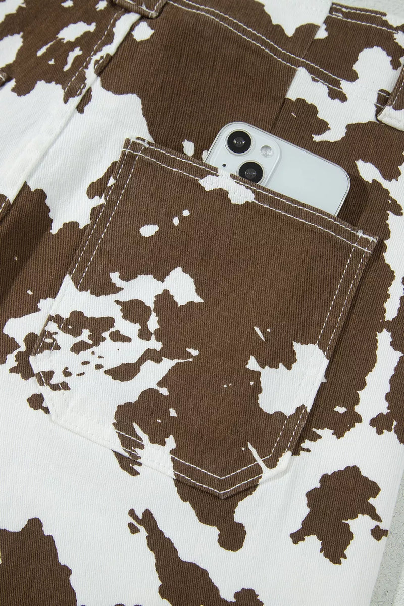 Close-up of a brown and white cow-print garment with a front pocket holding a white smartphone.