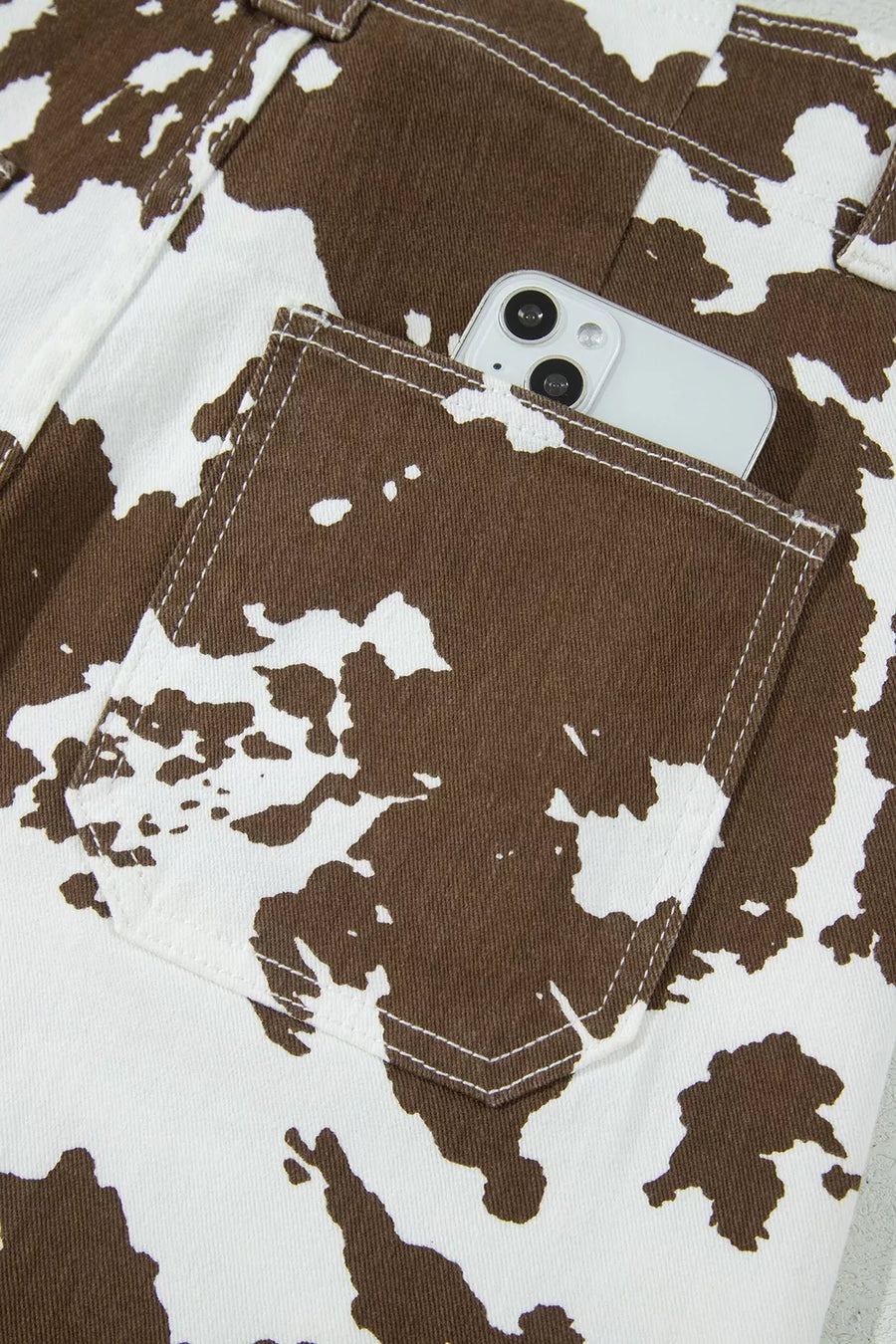 Close-up of a brown and white cow-print garment with a front pocket holding a white smartphone.