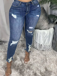 Person wearing distressed blue jeans standing on a textured surface with a neutral background