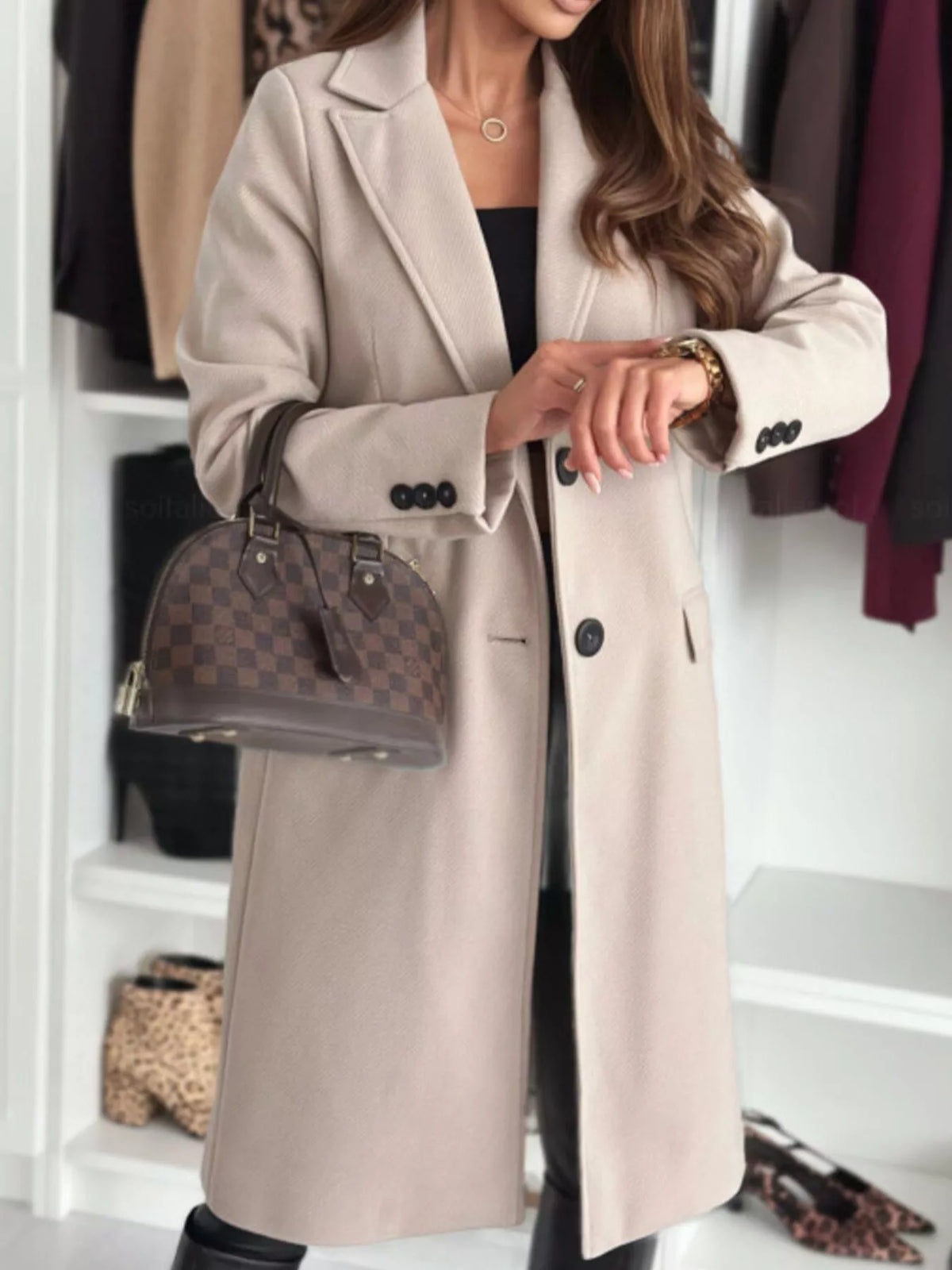 Person wearing a beige coat with a patterned handbag in a closet setting