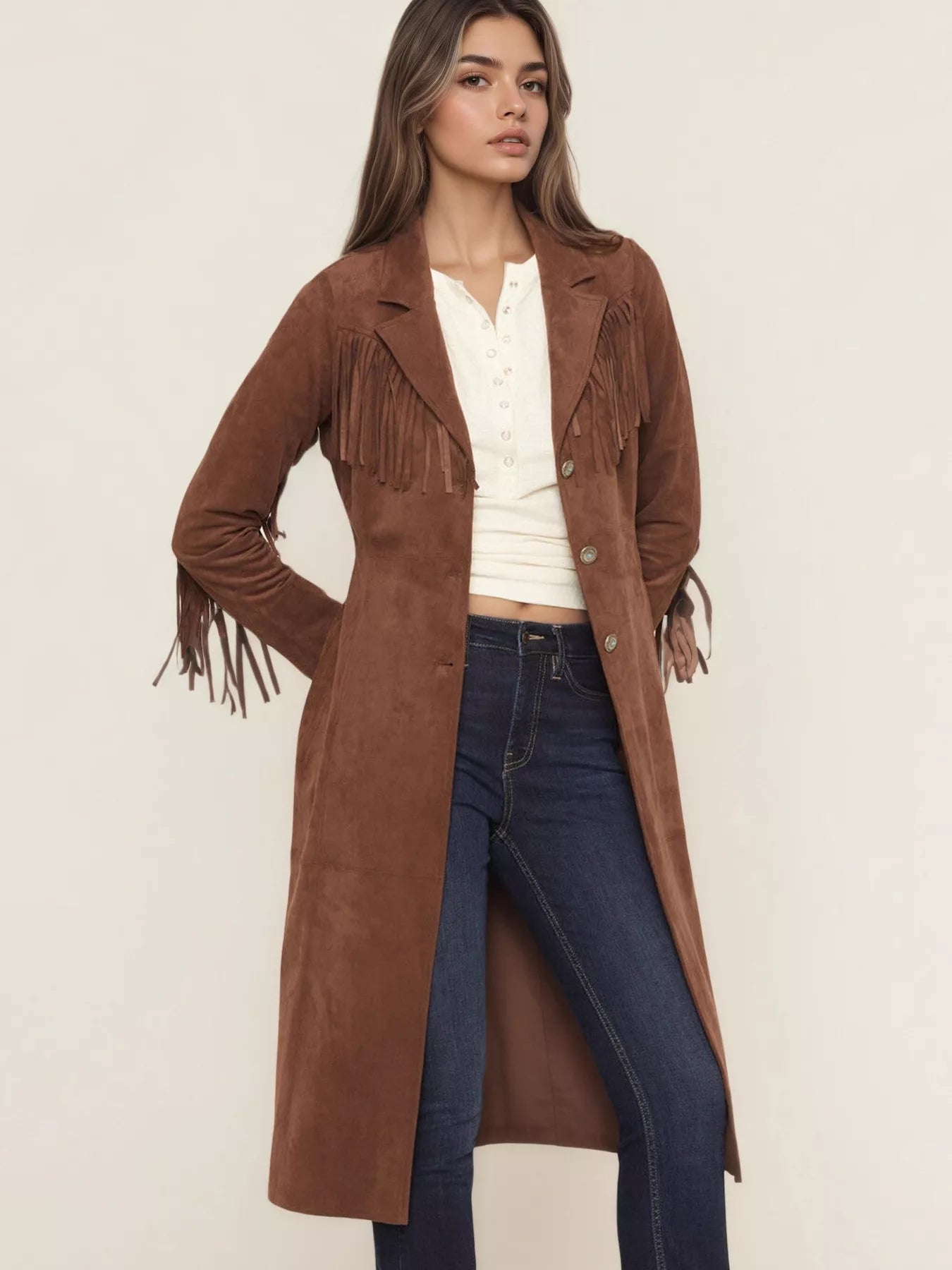 Woman wearing a brown suede coat with fringe details on a plain background