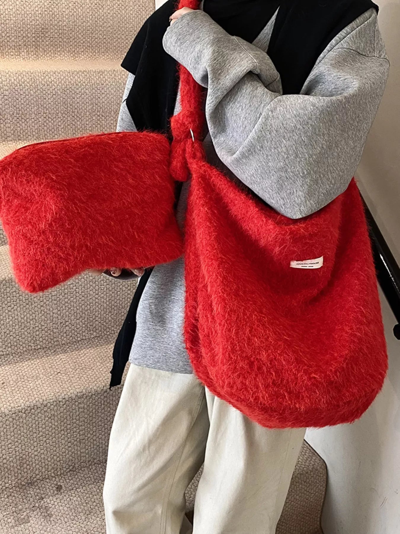 Person holding a red fluffy bag with a brand logo indoors.