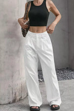 A woman wearing white wide-leg pinstripe pants with a black crop top, holding a leopard-print shoulder bag, standing against a textured concrete wall.