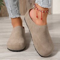 Beige clogs worn with denim jeans on a wooden floor.