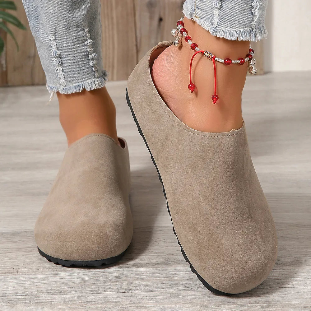 Beige clogs worn with denim jeans on a wooden floor.