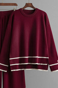 Burgundy sweater with white stripes on a hanger against a gray background