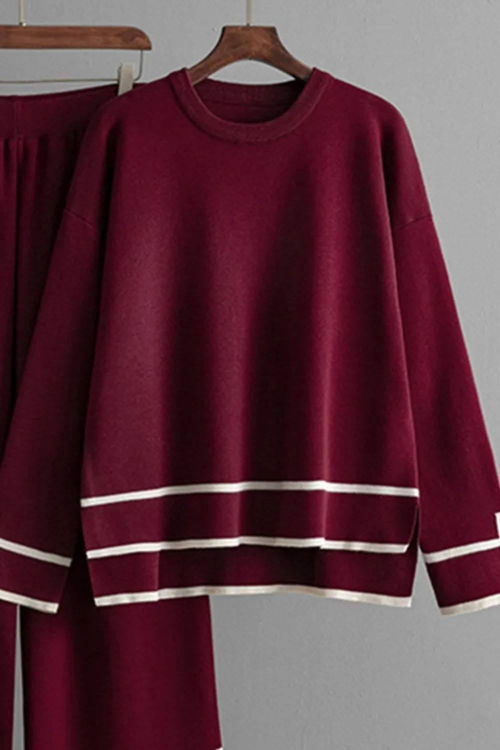 Burgundy sweater with white stripes on a hanger against a gray background