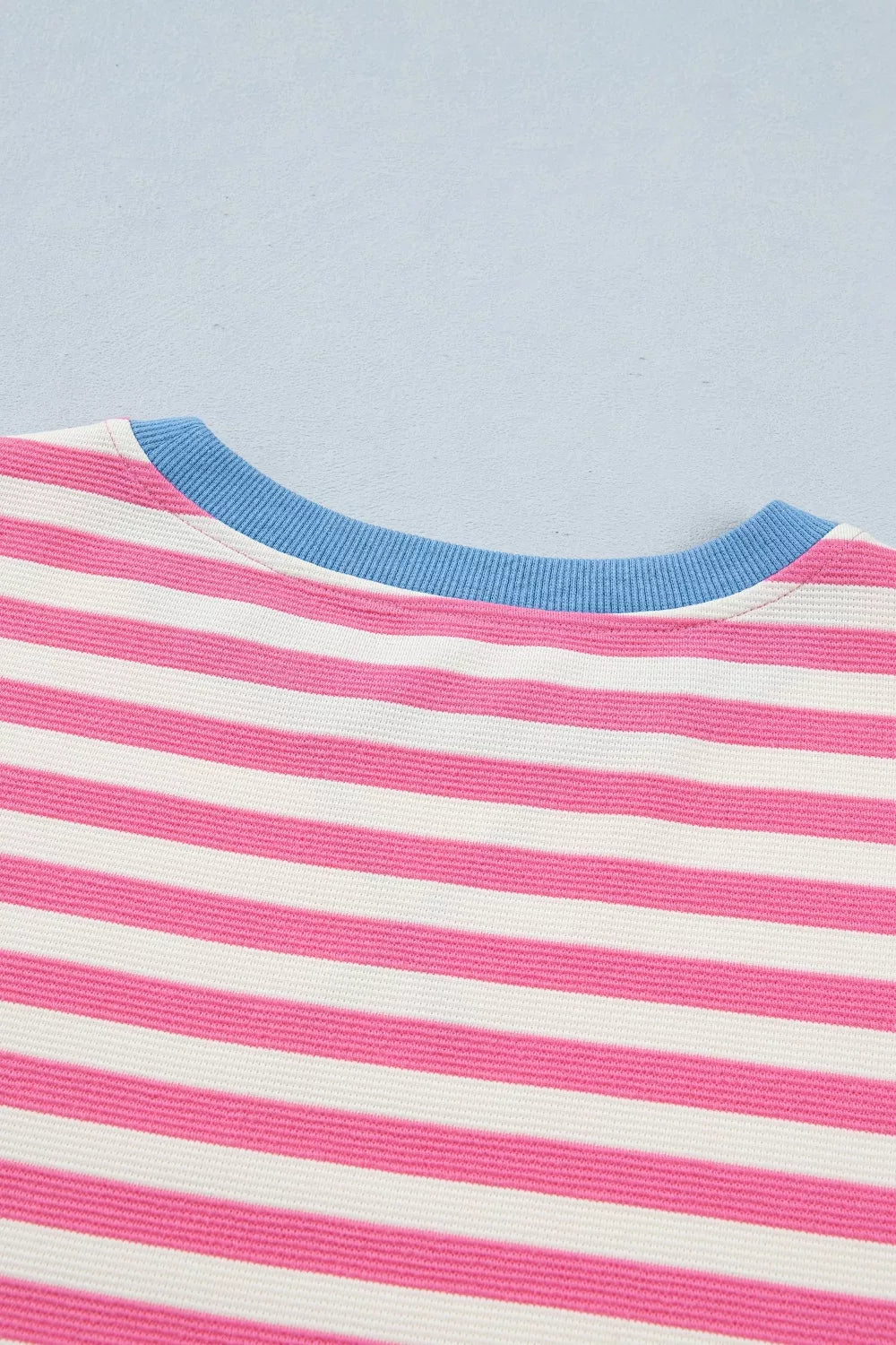 Close-up of a shirt with pink and white stripes and blue neckline against a light blue background