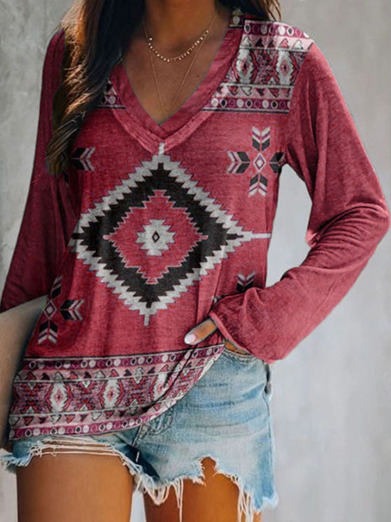 Person wearing a red patterned long-sleeve shirt and denim shorts against a neutral background