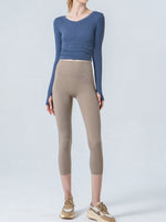 Person wearing a blue long-sleeve top and beige leggings on a white background