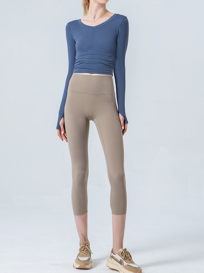Person wearing a blue long-sleeve top and beige leggings on a white background