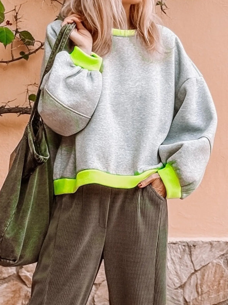 Person wearing a gray sweatshirt with neon green accents and holding a green bag against a stone wall.