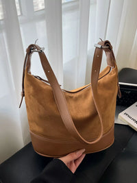 Brown handbag held by a person with a light curtain background