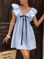 Woman wearing a blue and white striped dress with a bow detail, standing against a wooden background.