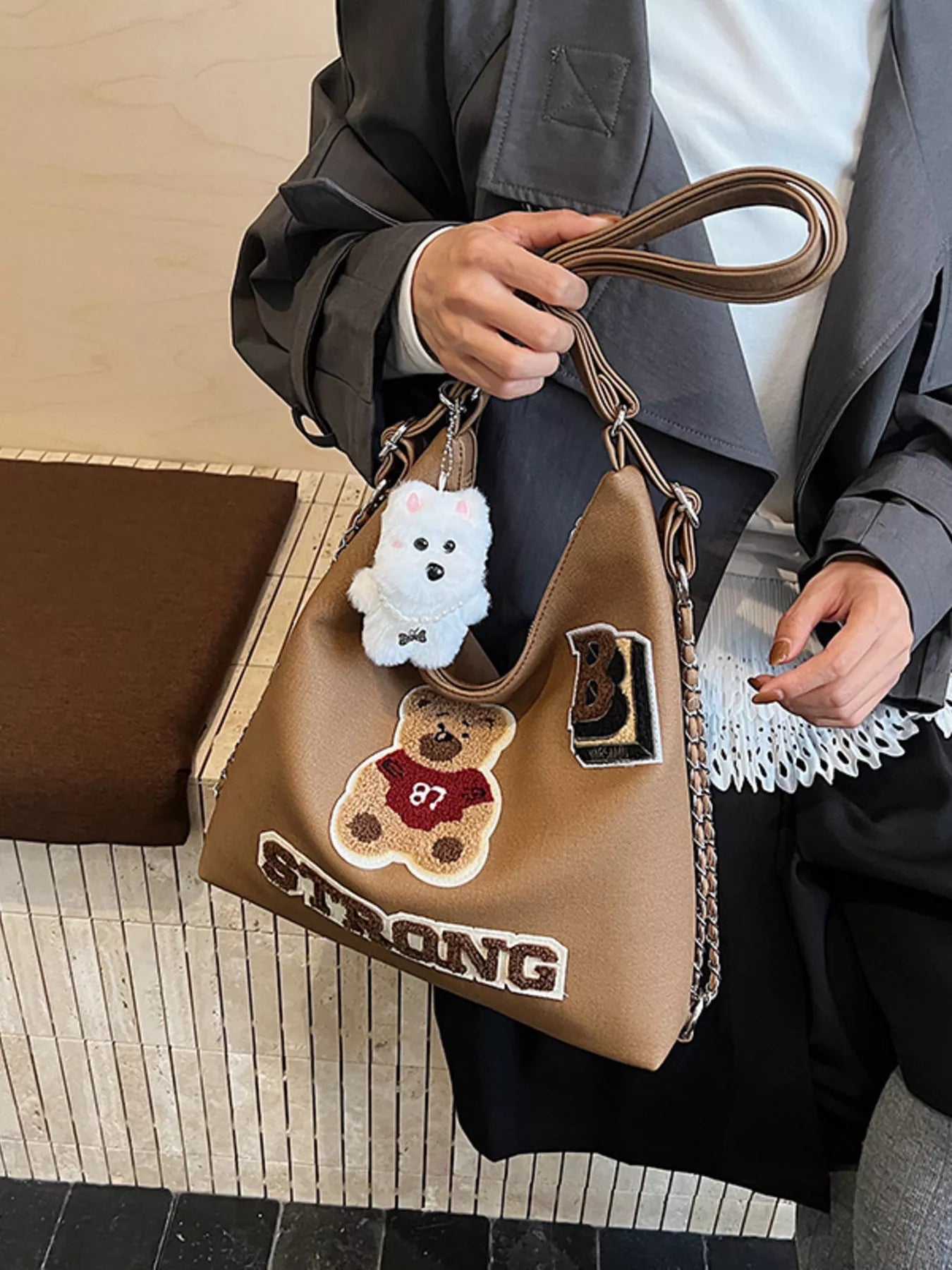 Person holding a brown handbag with teddy bear designs and 'STRONG' text.