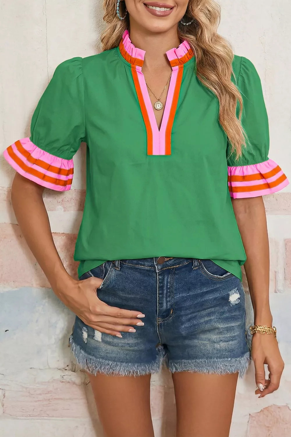 Woman wearing a green blouse with colorful cuffs and denim shorts against a light background