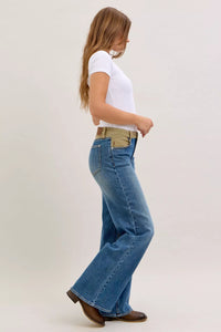 Woman wearing blue flared jeans and a white top on a plain background