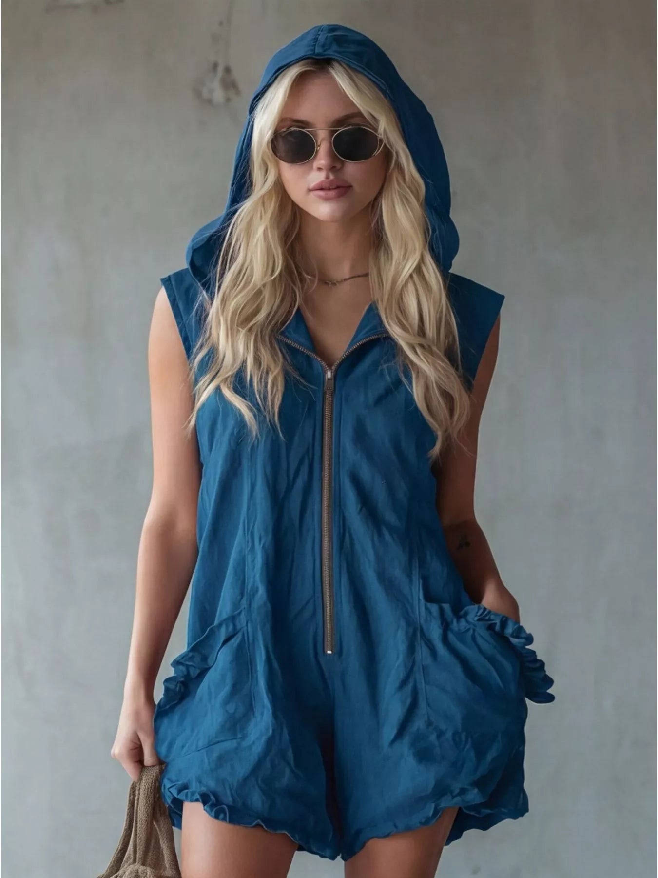 Woman wearing a blue sleeveless hooded romper against a plain background