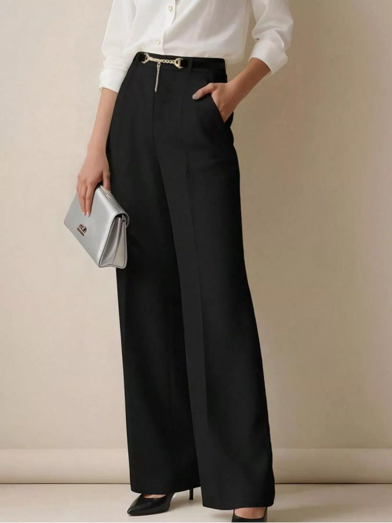 Person wearing a white shirt and black wide-leg pants holding a silver clutch against a beige background