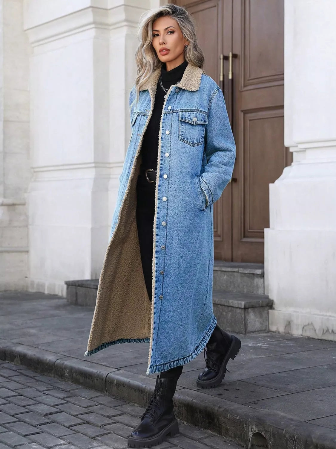 Woman wearing a long denim coat with fur trim standing on a street.