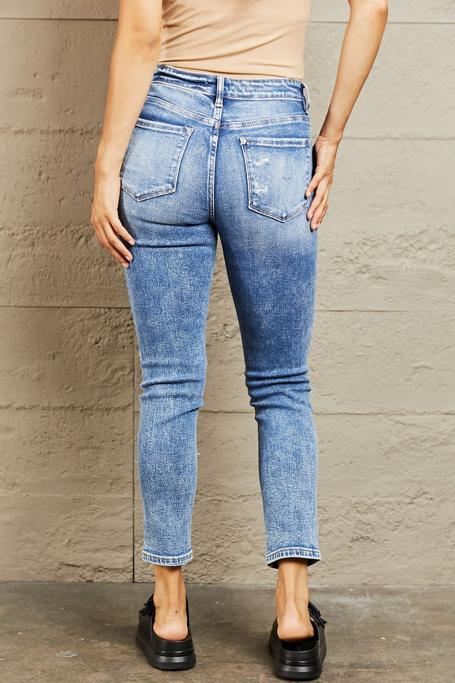 Person wearing blue jeans against a beige wall