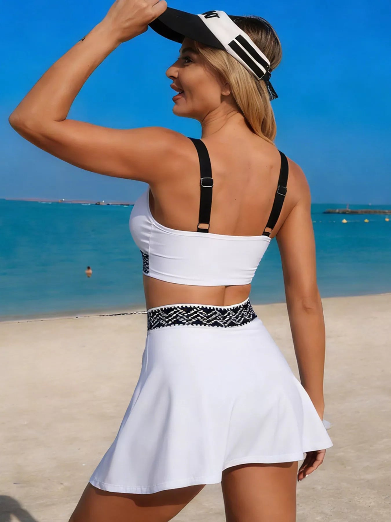 Woman in a white bikini and skirt on a beach with clear blue water and sky.