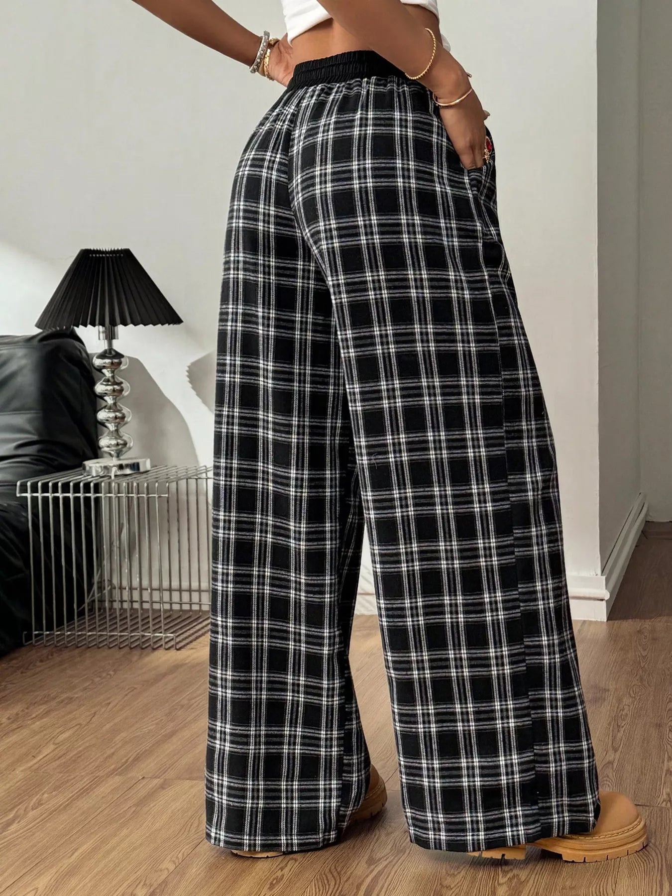 Person wearing black and white plaid pants in a room with a lamp and sofa.